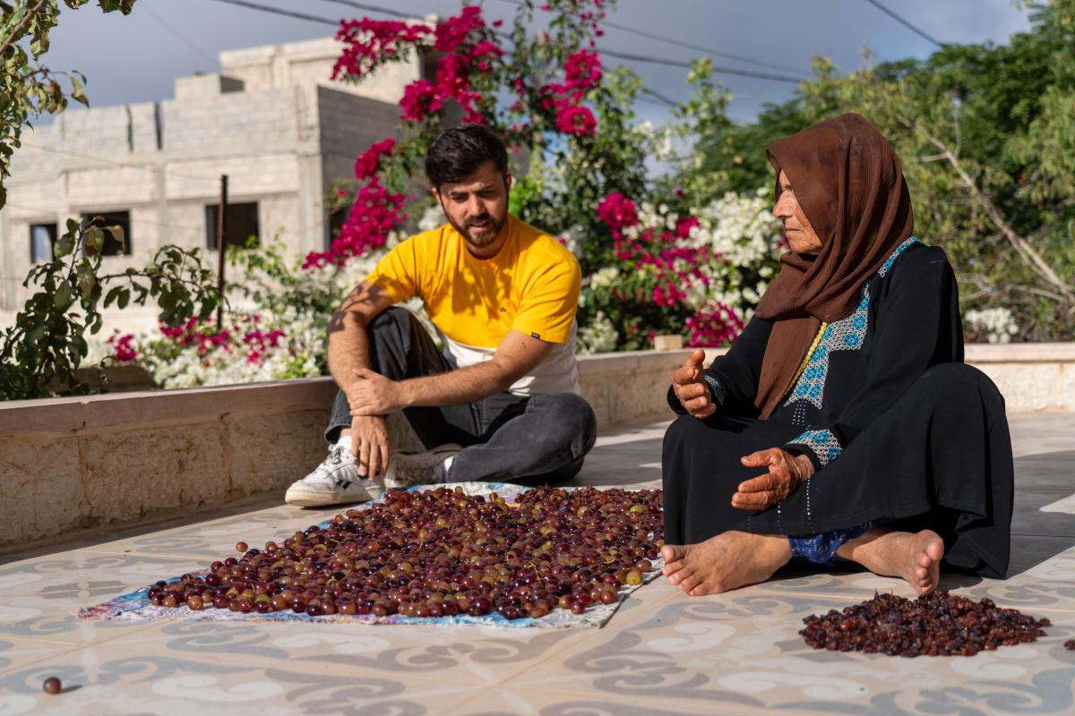 Hareth Yousef and his grandmother sit outside next to a pile of sour cherries