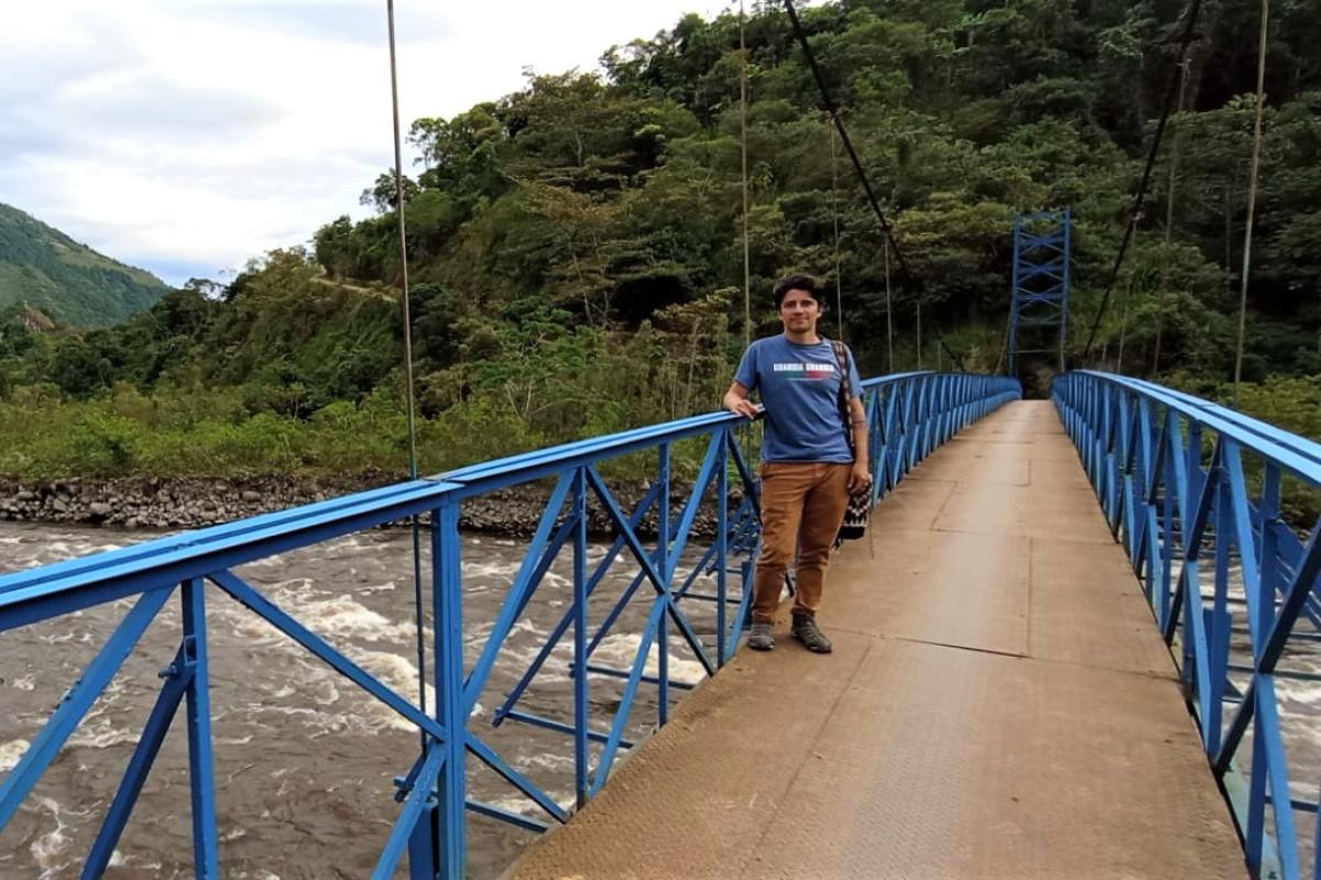 John Sabogal Venegas stands on a bridge over a river in the mountains of Colombia